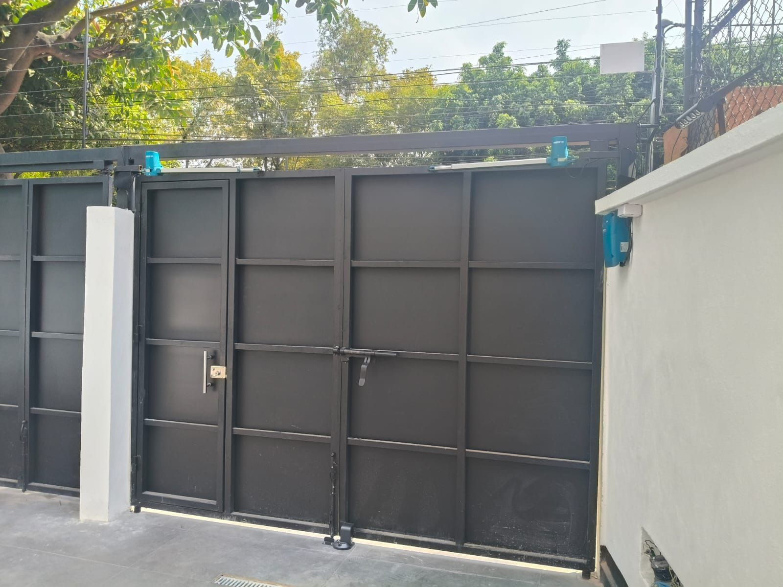 Portón negro de lámina con puerta peatonal y pistones